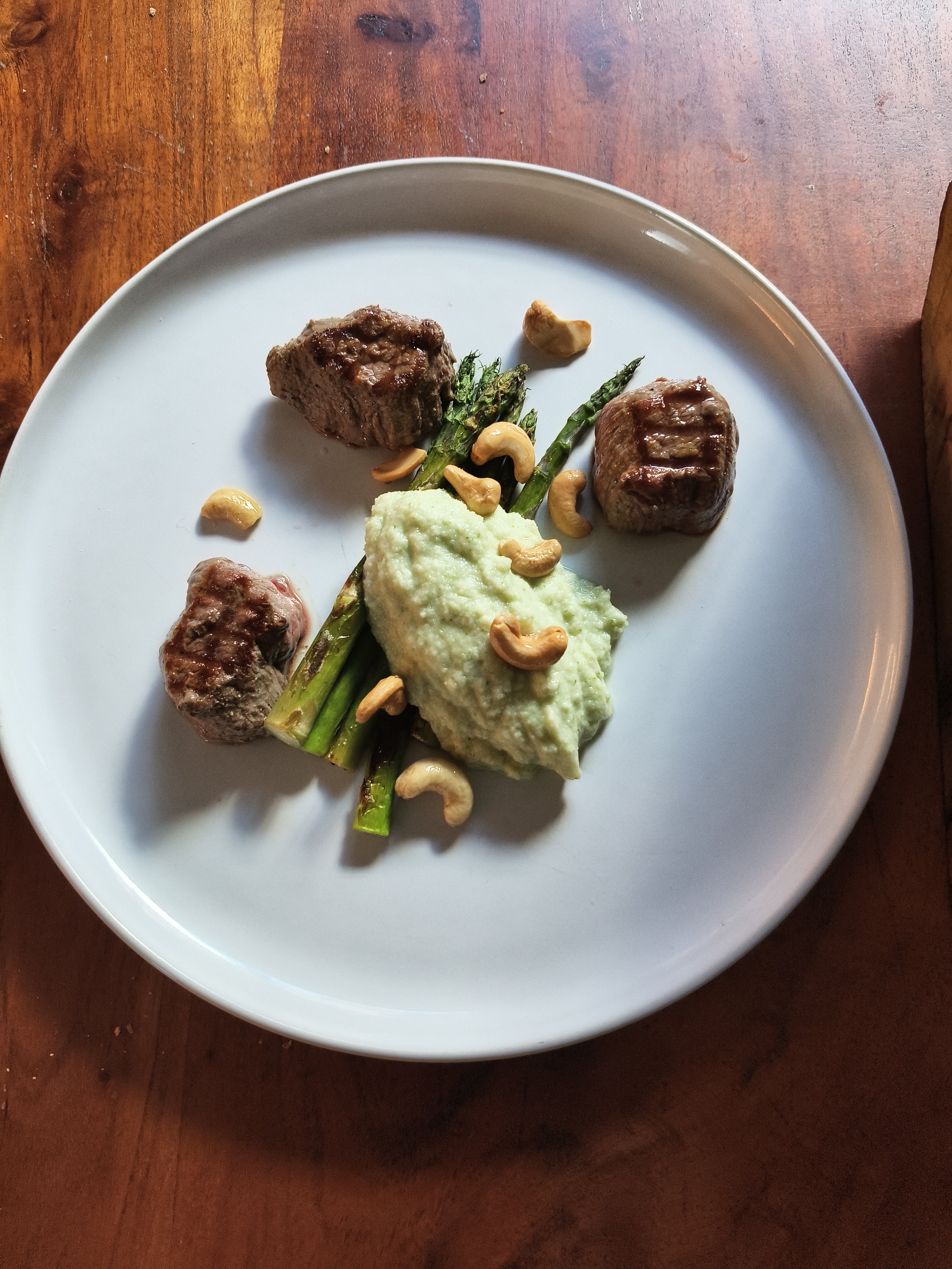 Bord met asperges, cashewnoten en een groene saus op een houten ondergrond voor een home dining prive chef experience